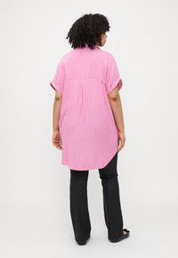 Pink and white striped short-sleeve shirt with a curved hem and buttoned back. Paired with black fitted pants and flat shoes.