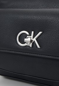 Borsa in pelle nera con texture, caratterizzata da un importante logo argento con elementi circolari e rettangolari. Design pulito e moderno.