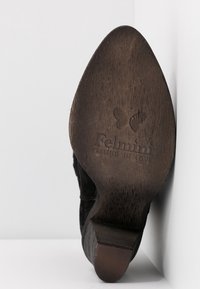 Suela de zapato de madera con forma curva y puntiaguda. Parte superior de ante negro con detalles de costura y logotipo embosado, "FELMINI FALLING IN LOVE."
