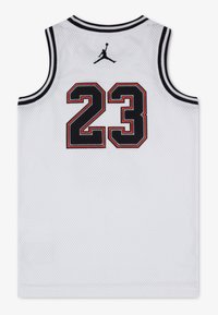 Λευκή μπασκετική φανέλα από δίχτυ με μαύρες και κόκκινες λεπτομέρειες. Φέρει τον αριθμό «23» με έντονη γραμματοσειρά και ένα μαύρο λογότυπο Jumpman πάνω από τον αριθμό.