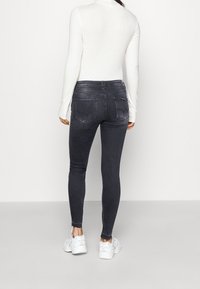 Jeans ajustados negros con bolsillos traseros, combinados con una camiseta de manga larga blanca y zapatillas blancas. Tejido suave con un diseño entallado.