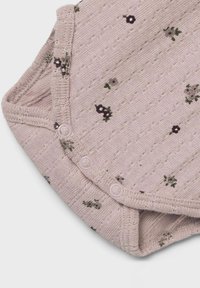 Un body pour bébé tricoté rose avec un motif texturé orné de petites impressions florales, trois boutons de fermeture et un col rond.