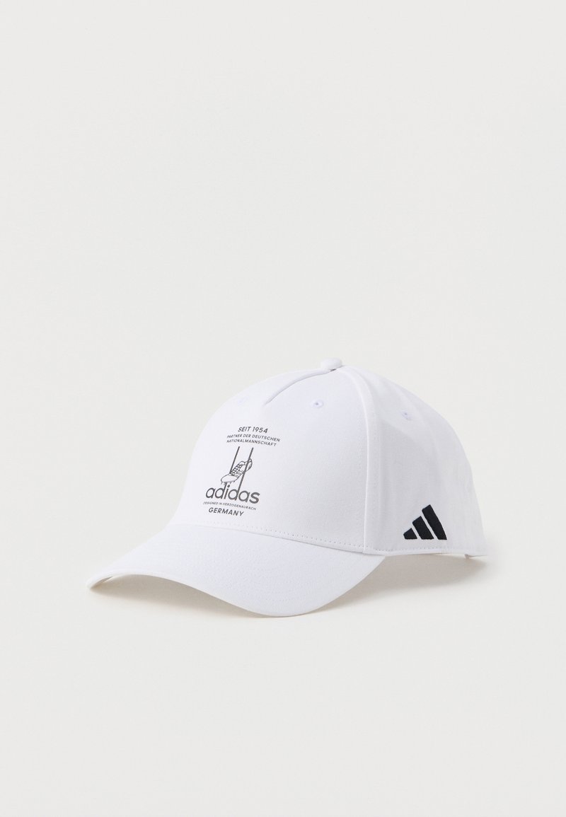 Balts Adidas beisbola cepure ar melnu logo un tekstu, kas minē "Kopš 1954" un Vācija, attēlota uz vienkārša fona.
