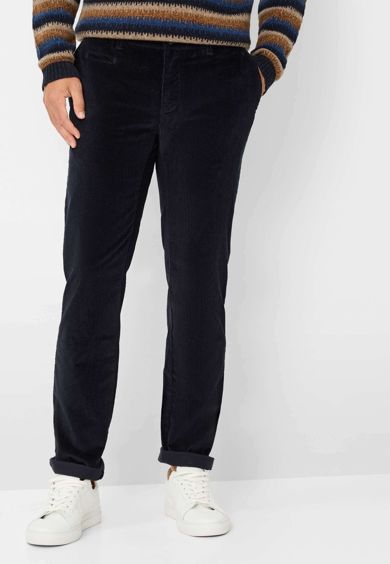 Marineblauwe corduroy broek met een rechte pasvorm, voorzien van voortassen en opgerolde manchetten, gecombineerd met witte sneakers.