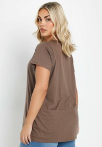 Brun kortærmet t-shirt med en afslappet pasform, blød tekstur og en let buet kant, båret med blå denim jeans.