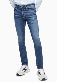 Modré denimové džíny s úzkým střihem, klasickým pětizkrovým designem, kontrastním šitím a opotřebovanou texturou.