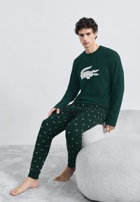 Parte superior de pijama de manga larga verde con gráfico de cocodrilo blanco y pantalones de pijama verdes estampados con pequeños cocodrilos blancos. Ajuste suave y casual.