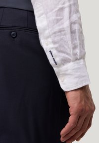 Biała koszula lniana z zapięciami na guziki, z granatowym haftem. W połączeniu z ciemnymi spodniami z tkaniny, prezentującymi elegancki, dopasowany wygląd.