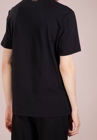 Camiseta de algodón negra con mangas cortas, cuello redondo y un diseño liso. Sin patrones visibles ni elementos metálicos; silueta simple y entallada.