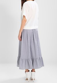 Biała bluzka z krótkim rękawem, zestawiona z niebiesko-białą spódnicą midi w paski z falbaną na dole, noszona z białymi botkami za kostkę.