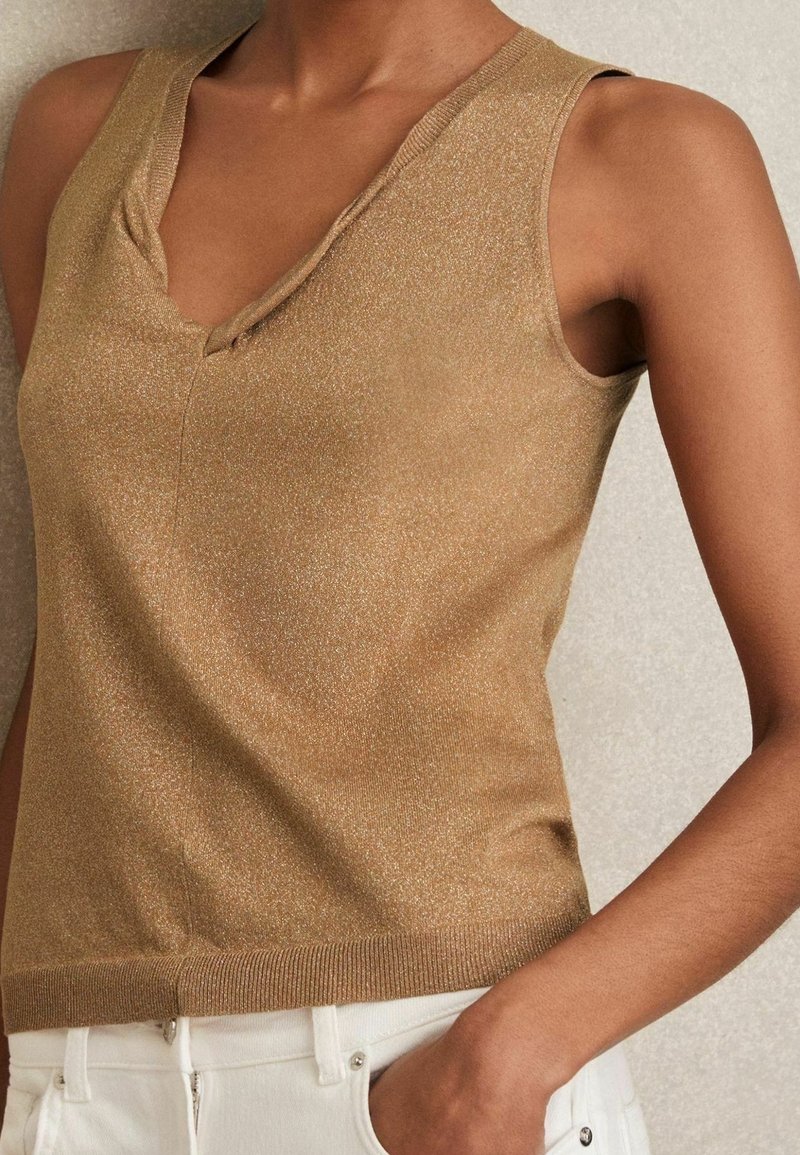 Beżowy top na ramiączkach z delikatnym połyskiem, z dekoltem w serek i dopasowanym dołem sięgającym talii. Teksturowana tkanina z żebrowanymi akcentami.