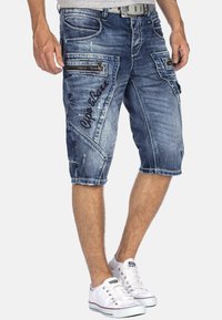 Shorts cargo en denim bleu clair avec un effet délavé, logo brodé et plusieurs poches zippées. Dispose d'un ourlet effiloché et d'une coupe décontractée.