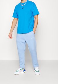 Blå bomullströja med Nike-logga, kombinerad med ljusblå joggingsbyxor och vita sneakers med flerfärgade detaljer.