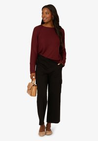 Bordeauxfarbenes geripptes Sweatshirt, schwarze weit geschnittene Hose und beiger Handtasche. Rutschfeste Schuhe mit gewebter Textur. Schlichtes, lässiges Design mit Taschen.