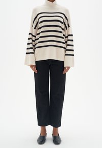 Krämfärgad och svart randig polotröja med vida ärmar, tillsammans med höga svarta raka jeans och svarta slip-on skor.