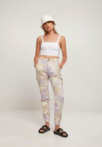 Cargo bukser i beige med lilla camouflagemønster, elastiske manchetter og sidelommer, parret med en hvid crop top og sorte sandaler.