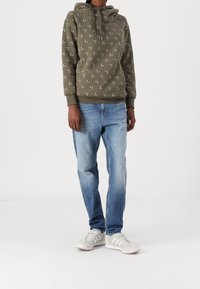Sudadera verde oliva con pequeños patrones florales, combinada con jeans azul claro y zapatillas gris-blancas con detalles a rayas.