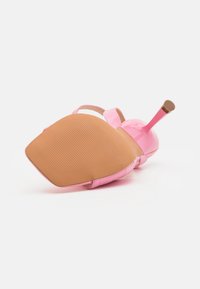 Vaaleanpunainen korkokenkä makaa kyljellään, näyttäen teksturoitua beigettä pohjaa ja ohutta stiletto-korkoa, jossa on kuminen kärki.