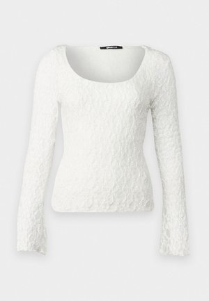 Vit spets långärmad topp med fyrkantig halsringning och utsvängda ärmar med ett texturerat blommönster genomgående.