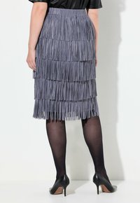 Jupe frangée grise avec plusieurs bandes superposées, tissu texturé, taille élastique, associée à des chaussures à talons hauts noires et des collants transparents.