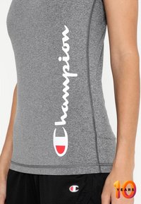 Camiseta de deporte gris con logo blanco de "Champion" y acentos rojos, hecha de una suave y elástica tela con costuras visibles.