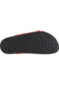 Semelle de chaussure avec une surface en caoutchouc noir texturé et un motif ondulé, bordée de rouge vif, conçue pour offrir adhérence et durabilité.