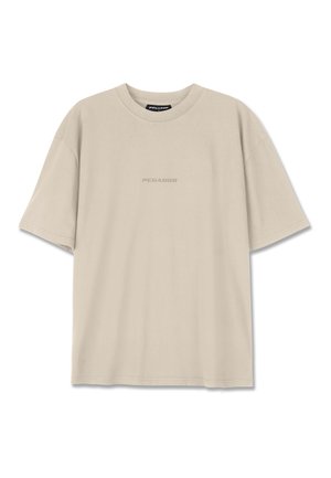 Camiseta de algodón beige con mangas cortas, escote redondeado y un sutil logo en relieve "PEGADOR" en el frente. Textura suave.