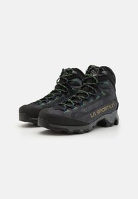 Bottes de randonnée noires avec des accents verts et jaunes, dessus texturé, embout renforcé et semelles extérieures robustes pour une bonne adhérence. Marque : La Sportiva.