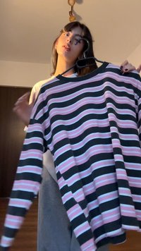 Majica z dolgimi rokavi in okroglim izrezom, okrašena s horizontalnimi črtami v črni, roza in svetlo modri barvi. Material deluje mehak, s sproščenim krojem.