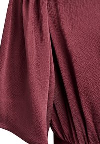 Mørkerød tekstureret stof med et draperet design, der har folder og en blød, let krøllet overflade, der fremhæver materialets dybde.