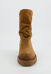 Botte en daim marron allant jusqu'aux genoux avec un design flou, un bout rond et une semelle en caoutchouc texturé présentant des détails en zigzag le long du bord.