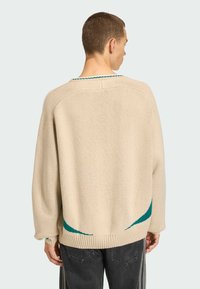 Beżowy sweter na drutach z luźnym krojem, z turkusowymi akcentami na dole i rękawach. Żebrowany dół dodaje tekstury i struktury.