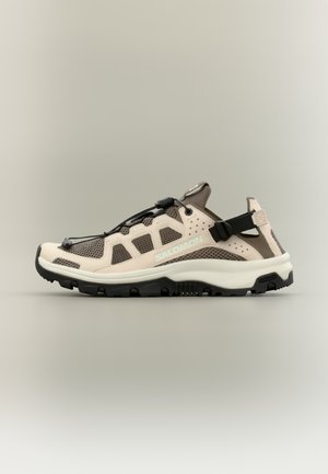 Beige and brown hiking sandal with breathable mesh, black adjustable strap, sturdy sole, and quick-lace system, branded Salomon on side.