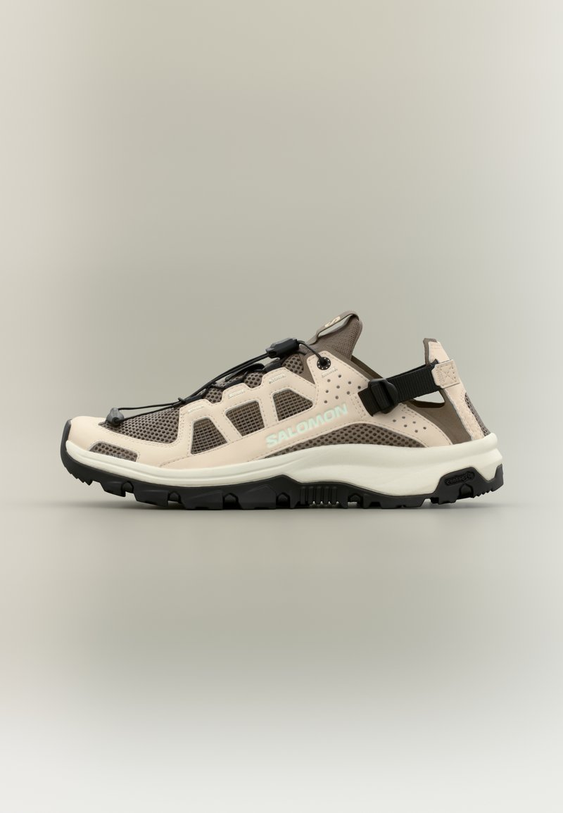 Sandale de randonnée beige et marron avec mesh respirant, bride noire ajustable, semelle robuste et système de laçage rapide, marquée Salomon sur le côté.