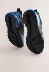 Zwarte sportschoenen met blauwe accenten, voorzien van een gestructureerde rubberen zool, gestroomlijnd ontwerp en een trek-lusje aan de hiel voor gemakkelijk aantrekken.