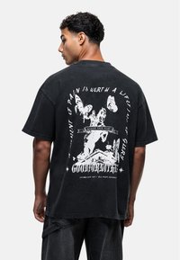 Black oversized t-shirt featuring a large white graphic design on the back, depicting a horse, butterflies, and text. Cotton material, short sleeves.