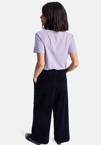 Lila T-Shirt mit kurzen Ärmeln, kombiniert mit schwarzen Corduroy-Hosen im weiten Schnitt, die eine lockere Passform und Seitentaschen bieten. Einfaches Design, weicher Stoff.