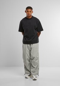 Črna prevelika bombažna majica s kroglo ovratnikom, v kombinaciji s svetlo sivo, ohlapno prilegajočimi se najlonskimi cargo hlačami. S funkcionalnimi elastičnimi manšetami in stranskimi detajli.