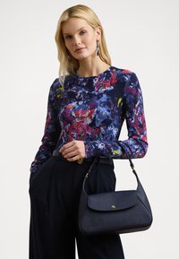 Floral-patterned long-sleeve top in dark blue, red, and yellow, paired with high-waisted black trousers and a structured black handbag.
