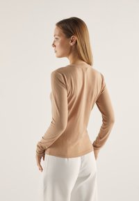 Langermet, tettsittende topp i et lett beige strikket stoff med vertikale ribbing. Har rund halsutskjæring og smale ermer.