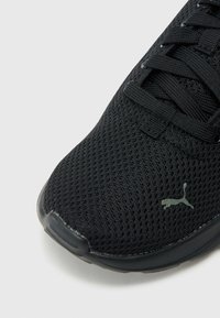 Juoda atletinė avalynė su tekstūruotu tinklinio viršumi, plokščiais raišteliais ir matinio juodo padais. Šone yra subtilus logotipas.