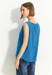Top azzurro senza maniche con una morbida trama e un dettaglio a chiave sul retro, abbinato a jeans blu scuro. Design semplice e moderno.