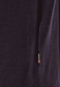 Dunkelblauer strukturierter Stoff mit einem kleinen schwarzen und roten Kleidungsetikett, auf dem "Club of Gents" steht und das in die Naht genäht ist.