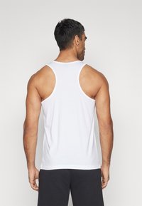 Camiseta sin mangas blanca hecha de tejido suave, con un corte clásico y un ribete de tela en contraste a lo largo de las sisas y el cuello.