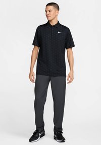 Black Nike polo shirt with a subtle dot pattern, short sleeves, and a collared neck, paired with dark gray pants and black athletic shoes.