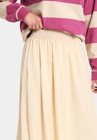 Licht beige lange rok met een geplooide tailleband en een zachte textuur, gecombineerd met een gestreepte trui in roze en crème.