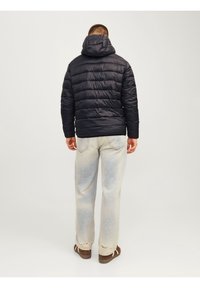 Marineblå boblejakke med hætte, quiltet design og elastiske manchetter. Stylet med lyse, slidte jeans og brune sko.