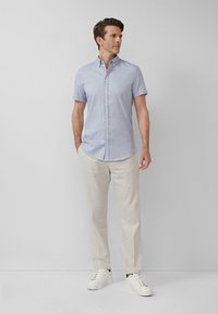 Lichtblauw kortmouw overhemd met een kraag, gecombineerd met beige linnen broeken en witte sneakers, tegen een neutrale achtergrond.
