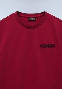 Bordeaux kurzärmliges T-Shirt mit rundem Halsausschnitt und einem gestickten schwarzen Logo auf der Brust. Weiche Baumwollqualität mit glatter Struktur.