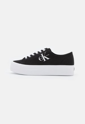 Black low-top canvas sneaker with white platform sole, white laces, and large "CK Calvin Klein Jeans" logo on side.